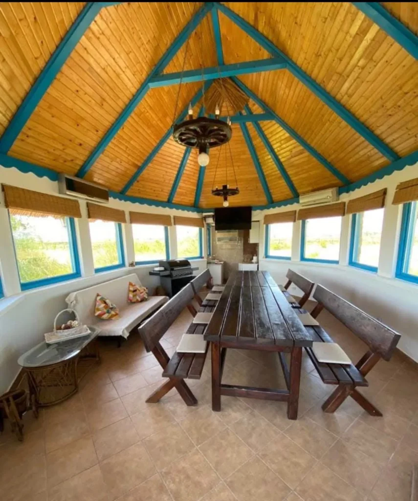 Wooden gazebo with table and benches, rustic interior.